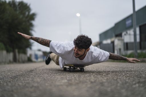 A cheerful European young male lying on skate and pretending to fly - concept of enjoying the life