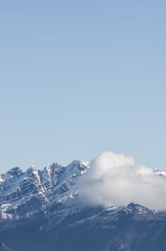 A vertical shot of a snow-covered rocky mountain partially covered with clouds