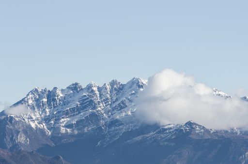 A view of a snow-covered rocky mountain partially covered with clouds