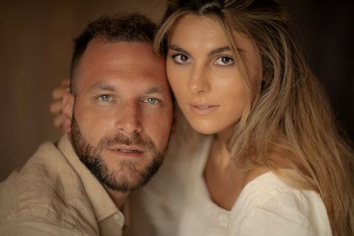 This image is of a man and woman posing together while both are wearing white shirts and brown hair