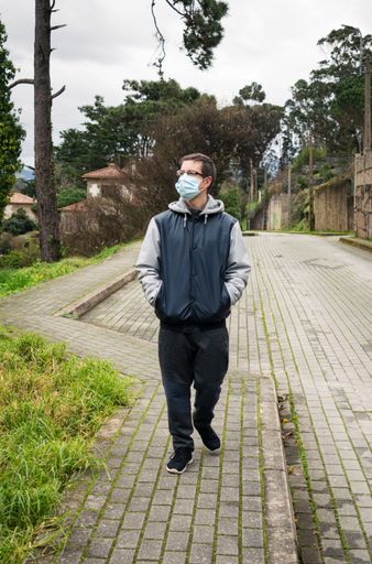 A vertical shot of a European tourist in glasses and facial mask walking down the street - new normal concept