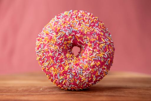 A closeup shot of a pink donut with colorful sprinkles