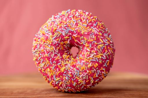 A closeup shot of a pink donut with colorful sprinkles