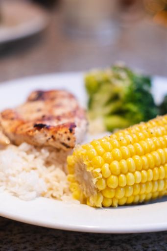 A vertical closeup shot of delicious roasted broccoli, chicken, rice, and corn