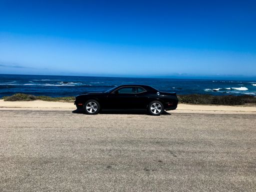 a black car in front of the blue ocean. although you can see some waves
