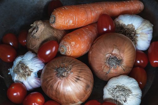 A closeup of fresh carrot, cherry tomatoes, garlic, and onions in a metal bowl