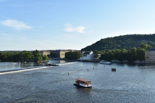 The boats in a river surrounded by forested mountains and old buildings in Prague