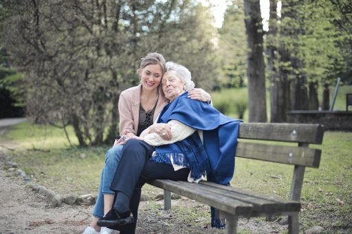 A granddaughter sitting on a bench in a park with her grandmother and hugging her
