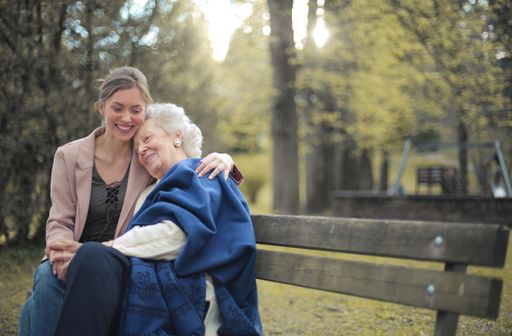 A granddaughter sitting on a bench in a park with her grandmother and hugging her