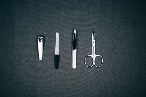 A high angle shot of tweezers, scissors, nail clippers, and nail art equipment on a black surfac