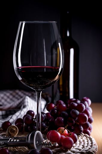 A vertical shot of a glass of red wine and grapes on a table