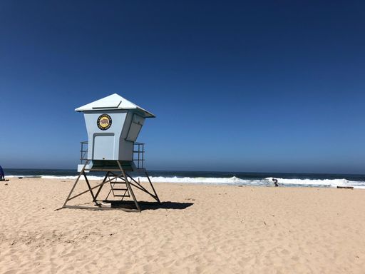 A lifeguard tower stands in silhouette against a serene beach backdrop, with a tranquil ocean stretching out in the distance