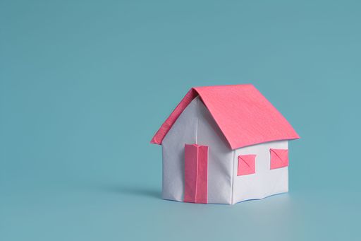 A miniature origami paper house with a pink roof against a blue background