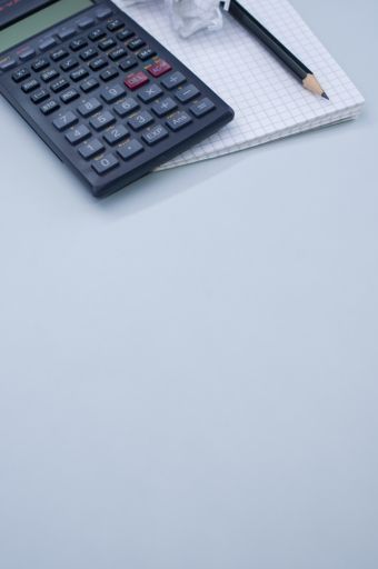 A vert shot of a calculator, a notepad and a pencil isolated on gray background