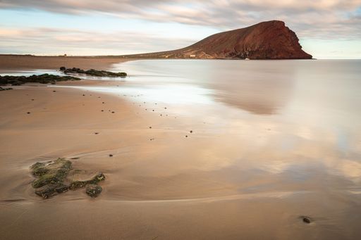 the beautiful scenery of the sea with a large rock in the background under the cloudy sky