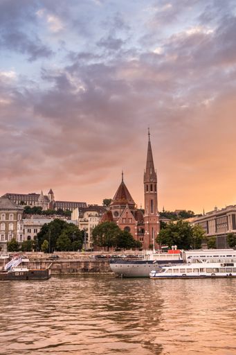 a beautiful vertical view of buildings and sea in the background of colorful cloudy sky in Budapest