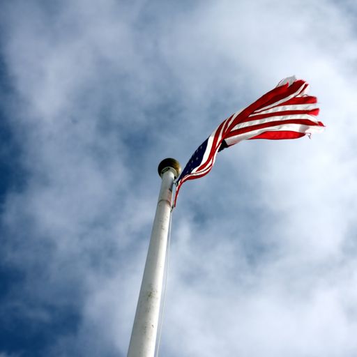 A low angle shot of a united states flag with a cloudy blue sky in the background