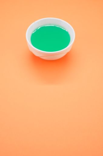 A vertical shot of a green watercolor in a bowl isolated on orange background