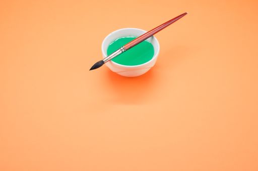 A closeup shot of a green watercolor in a bowl and a paintbrush isolated on orange background