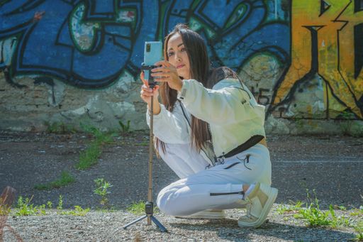 A young girl in a white tracksuit squatted down to set up her mobile phone to record a video of the history of a photo session against the wall