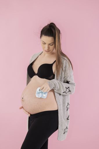 Young pregnant woman holding a pair of baby booties against her belly on a pink background. Pregnancy concept.