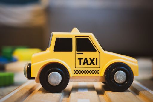 Yellow plastic toy taxi car on a wooden track in soft focus background
