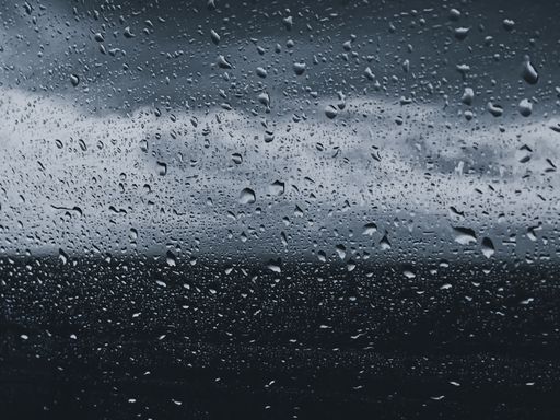 A closeup shot of a glass covered with raindrops on a blurred background