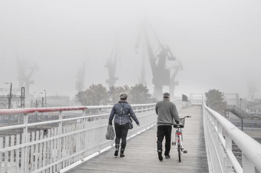A view of two-person walking on the footbridge in the shipyard in Gdansk, Poland against a foggy day