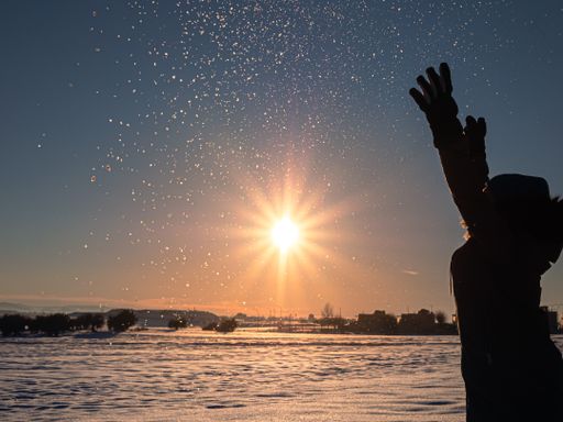 A silhouette of a woman throwing snow into the sky in a beautiful snowy field during the sunset