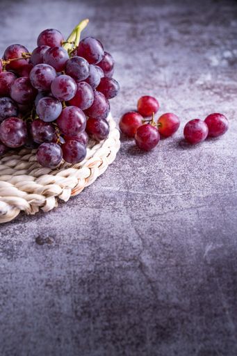 A vertical shot of red grapes on a board on a gray table