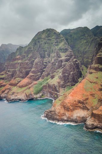 A beautiful aerial shot of the coast of Napali with clear beautiful water and steep rocks during a foggy day