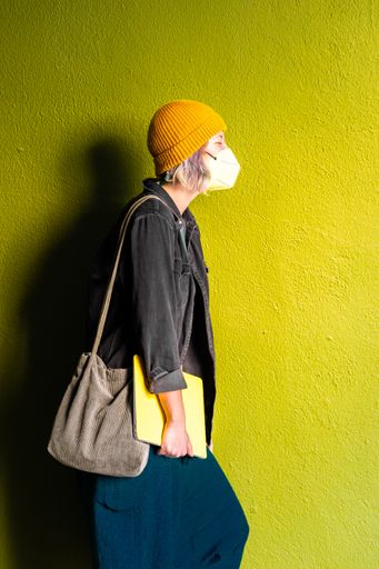 A Spanish student woman wearing a face mask while holding a yellow cased laptop - new normal concept