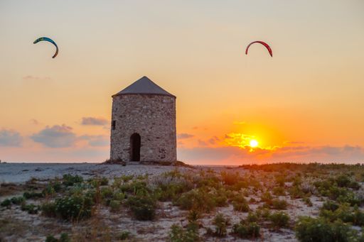 A beautiful view of Agios Ioannis Beach in Lefkada island with old windmill and kites in the sky at sunset