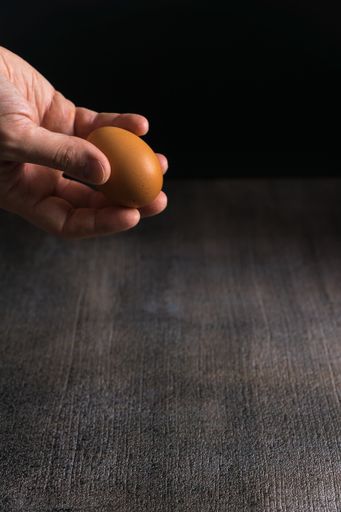 A closeup of a hand holding an egg ove a dark surface