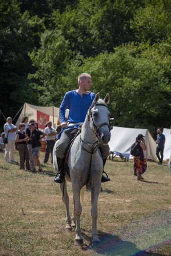 A man in a blue shirt sit on a horse and carry a sword
