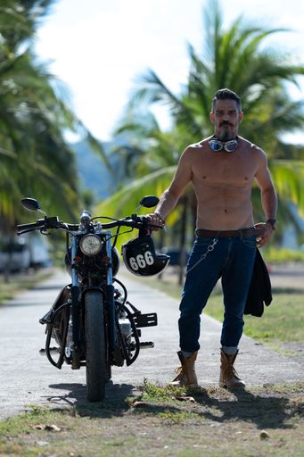 A sexy man with no shirt posing with his motorcycle in the palm pavement