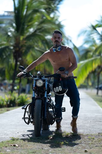 A sexy man with no shirt posing with his motorcycle in the palm pavement