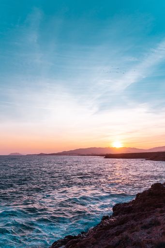 A beautiful view of a flock of birds flying over the peaceful sea under the breathtaking sunset sky