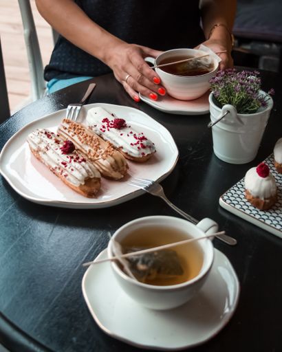 A vertical shot of a female eating French eclairs and drinking hot tea in a restaurant