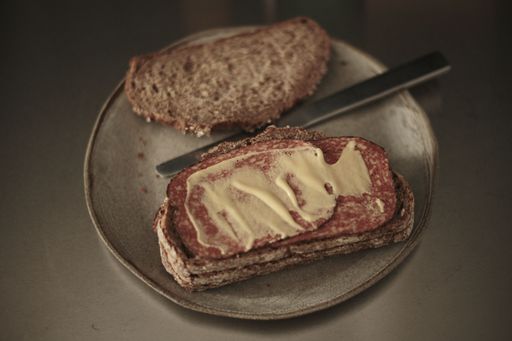 A white plate displaying two slices of fresh, white bread with a metal knife resting on the side