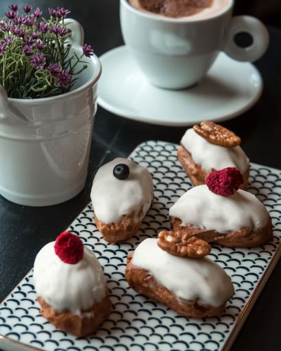 A vertical shot of French eclairs with white chocolate and a cup of coffee