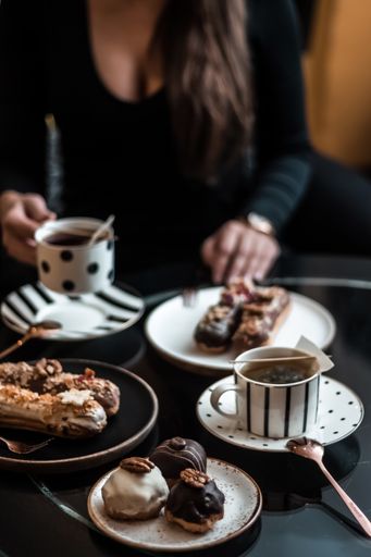 A vertical shot of a female drinking tea and eating French eclairs in a restaurant