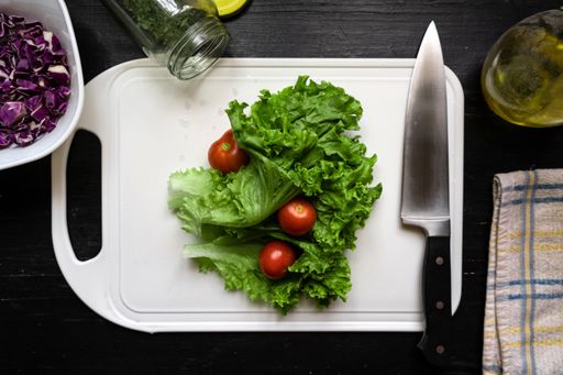 A top view of fresh lettuce and tomatoes on white cutting board with a knife