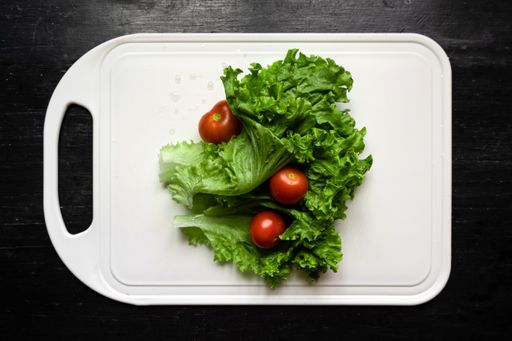 A top view of fresh lettuce and tomatoes on a white cutting board