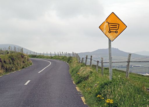 A yellow sign with a shopping cart on it on a side of a road