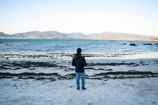 A back view of a man standing on the sandy beach and enjoying the view of the Ria de Vigo