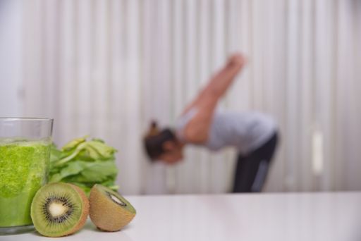 Green smoothie with focused kiwis and woman exercising on unfocused background