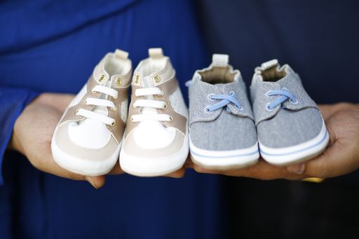 A closeup shot of future parents holding two pairs of baby shoes