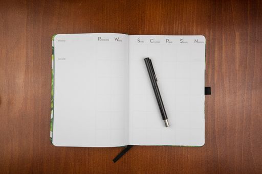 A top view of an open empty weekly dairy planner with a pen on a wooden table