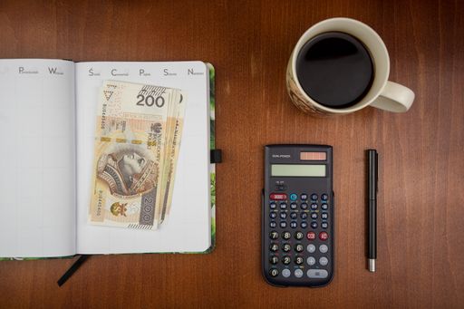 A top view of Polish 200 zloty banknotes on an open weekly dairy planner with office supplies and coffee on a wooden desk